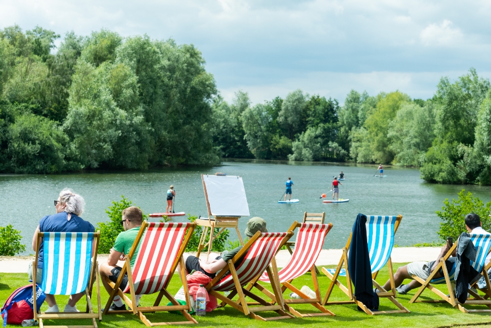 people in deckchairs watching paddle boarders on the lake