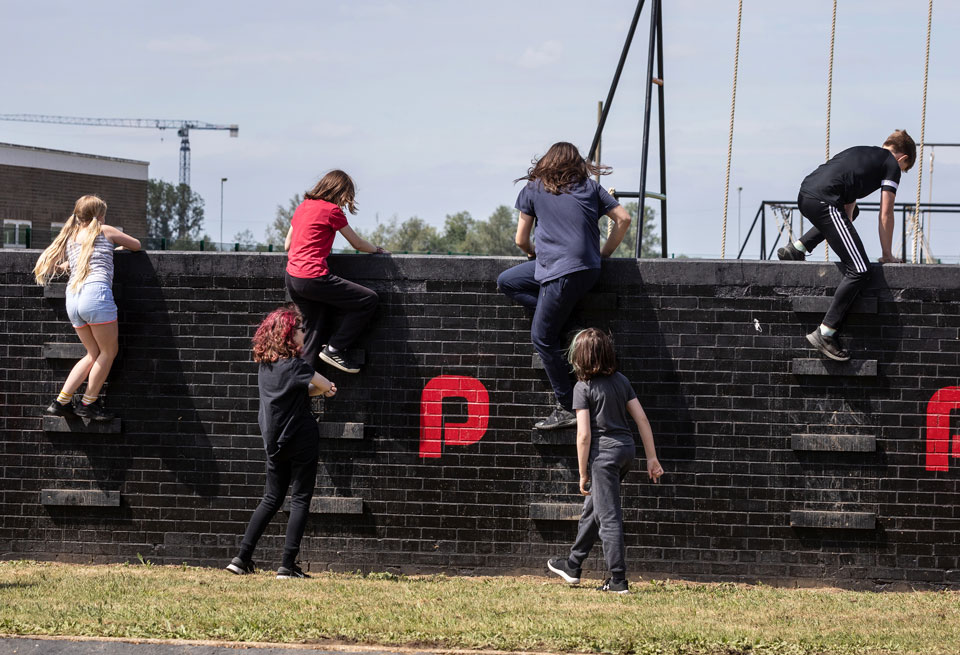 Children and young people climbing over a wall on the playground assault course
