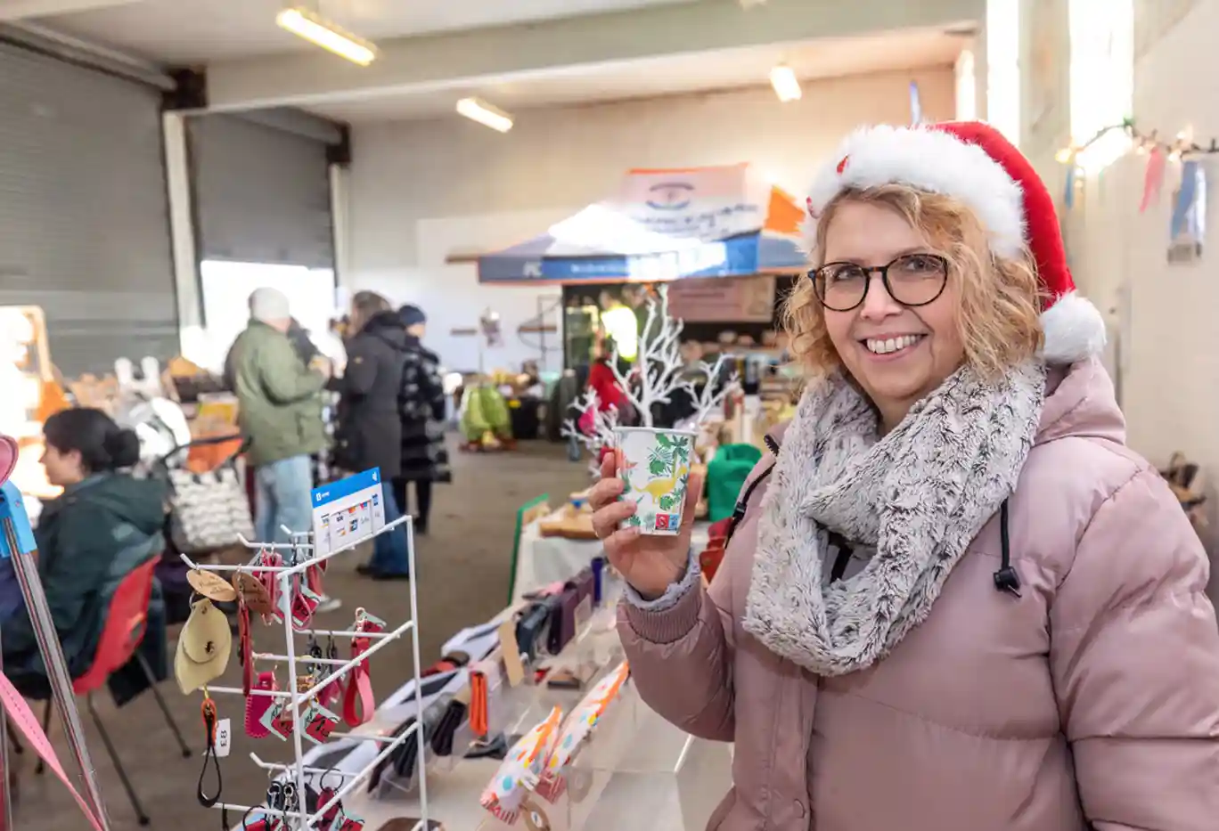 A smiling woman wearing a Santa hat with market stalls in the background at Waterbeach Christmas market.