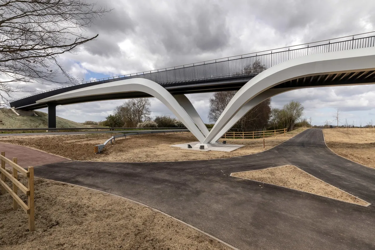New A10 bridge opens, completing predominantly off-road route between Waterbeach and Cambridge. Image shows the new bridge against a stormy sky